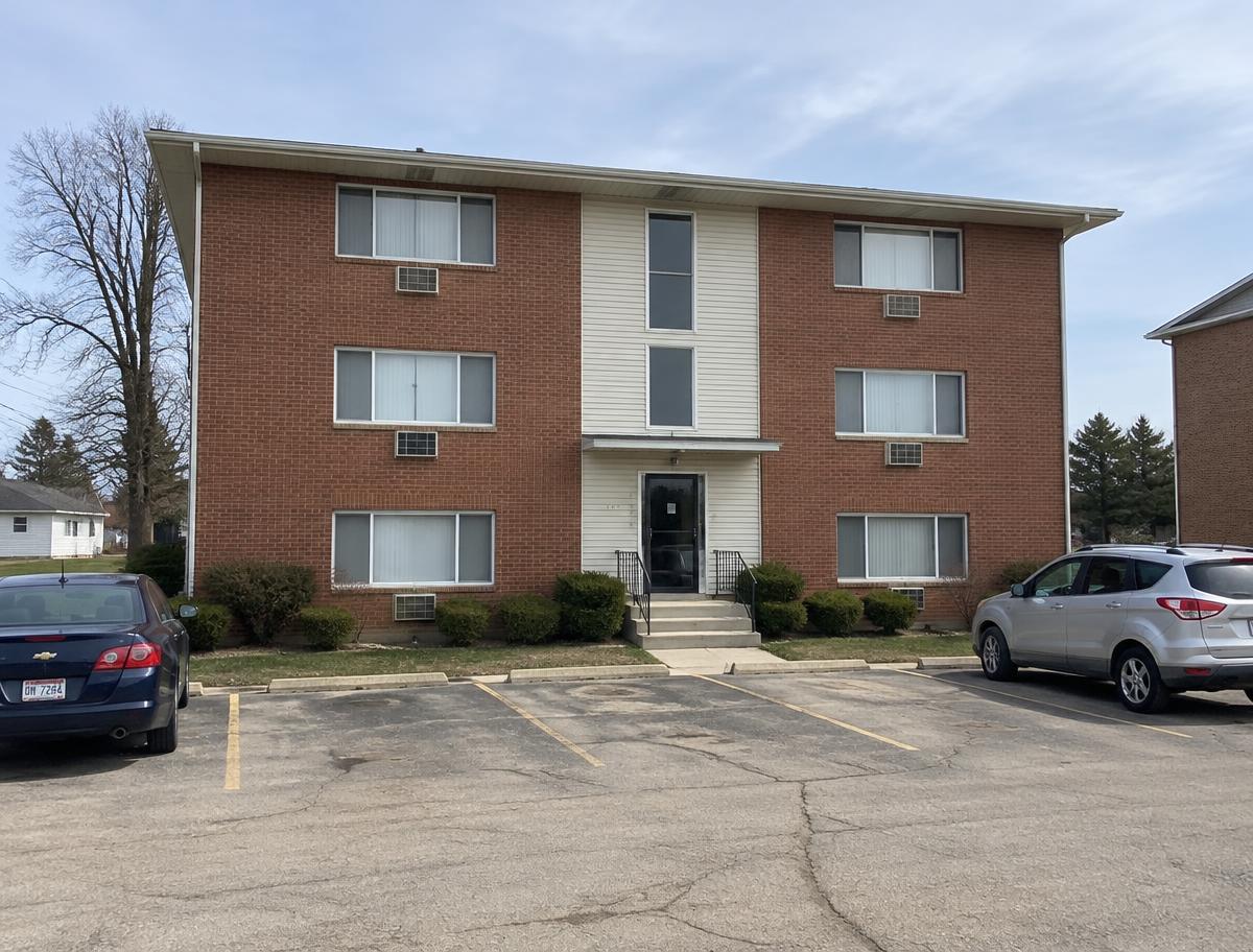 Illustrative photo: a plain three-story brick apartment building with a parking lot